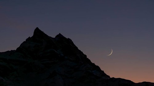 The crescent Moon gracefully hangs over the silhouette of the Dents du Midi mountain in the Swiss