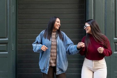 Joyful moment of a latin lesbian couple holding hands and laughing outside. Both wear casual