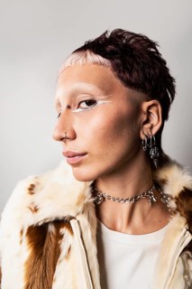 Wide angle close-up of a woman with a bold hairstyle, glamorous nose and ear piercings, striking