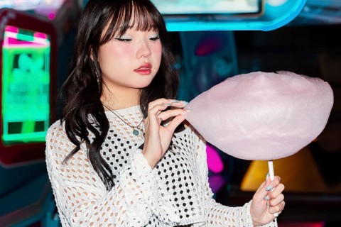 Asian Gen Z girl enjoys cotton candy in a vibrant arcade setting The colorful lights illuminate the