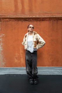 Stylish woman posing in a trendy fur jacket and sunglasses, set against a textured orange wall. The