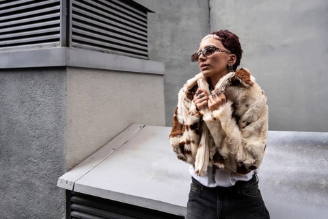 Stylish woman poses confidently in faux fur coat and sunglasses in an urban setting. Modern jewelry