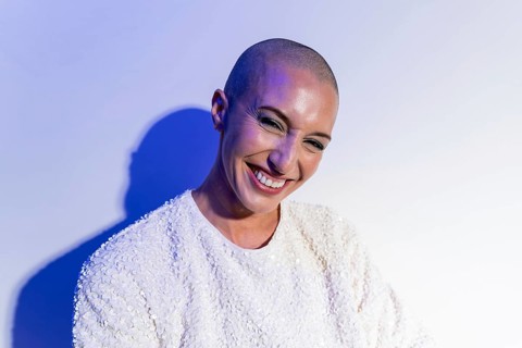 A middle-aged woman with a shaved head smiles confidently, reflecting self-assurance and