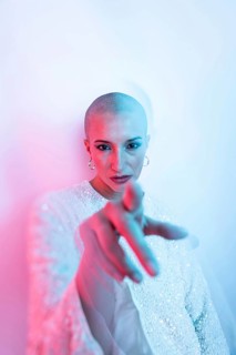 A middle-aged woman with a shaved head exudes confidence and style. She is pointing directly at the