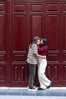 A loving latin lesbian couple shares a tender moment before a rich red wooden door. They embrace