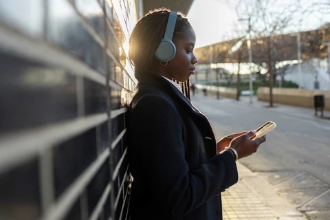 An African American businesswoman, sporting braids and headphones, is focused on her smartphone