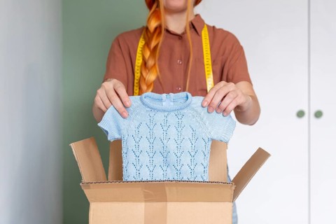A woman is organizing her closet, preparing clothes for online sale. She holds a blue knit sweater