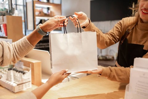A customer receives a shopping bag from a worker at a cosmetics store. The hands exchange