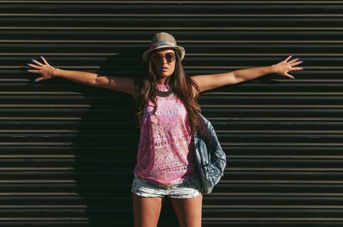 A fashionable woman poses confidently against a dark background, wearing a pink sleeveless top,