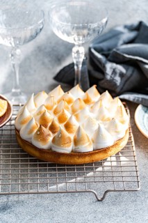 A beautifully baked a homemade lemon cake features toasted peaks, resting on a cooling rack.