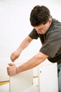 A focused young man assembles a new piece of white furniture using a screwdriver. He is seen