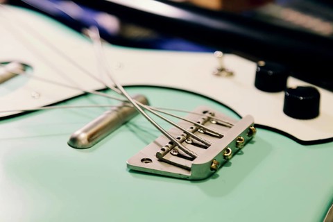 Close-up of a bass guitar bridge and strings in a luthier workshop. The focus is on the intricate