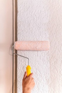 Cropped unrecognizable of a man's hand using a paint roller on a textured wall, capturing a moment