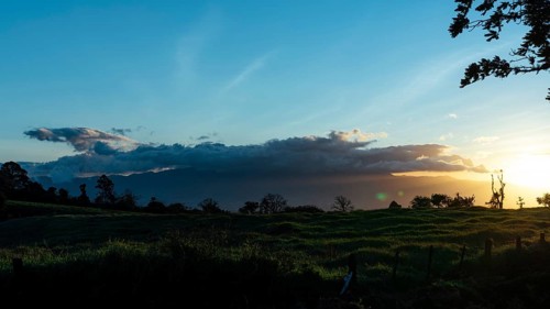 Capture the serene beauty of sunset over lush green fields under a vibrant sky lit by the