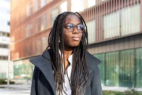 An African American businesswoman with braids and glasses takes a break outside a modern office