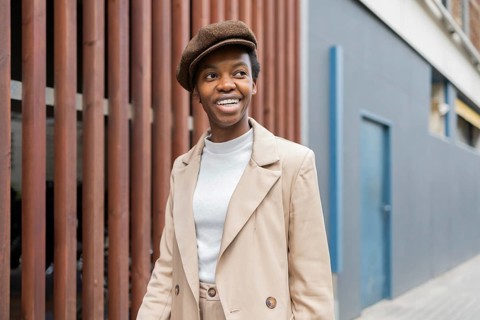 A black woman in an urban environment, wearing a stylish beige outfit paired with a beret She