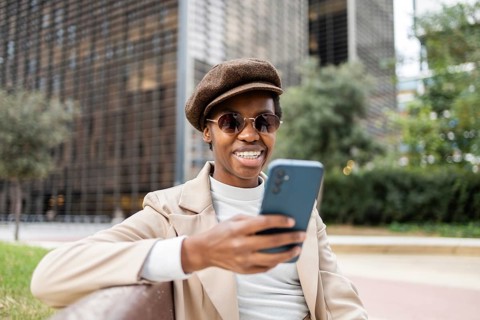 A stylish black woman wearing sunglasses and beret, sitting on a bench in the city She smiles while