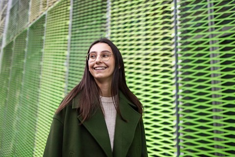 A woman in a stylish green coat smiles joyfully while standing against a vibrant, abstract green