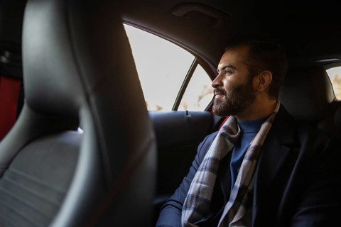 Indian male businessman dressed in formal wear with a winter scarf, traveling in the backseat of a