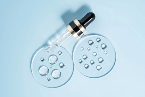 A pipette dropper with a skincare serum rests on a smooth, light blue surface Surrounding the