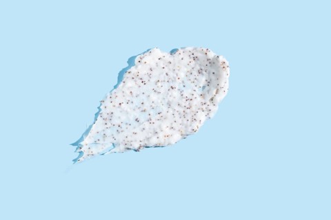 Exfoliating cream with microbeads smeared against a pale blue background, showcasing the texture