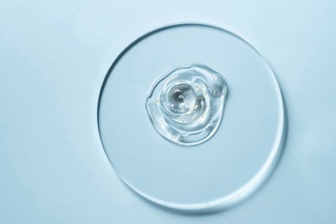 A clear gel with small golden specks on a round glass plate against a light blue background The