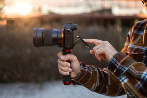 Close-up of hands holding a camera and adjusting the screen during golden hour The scene captures