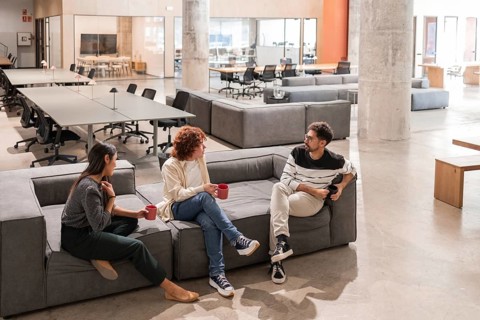 Three coworkers engage in a friendly and productive discussion in a modern office lounge,