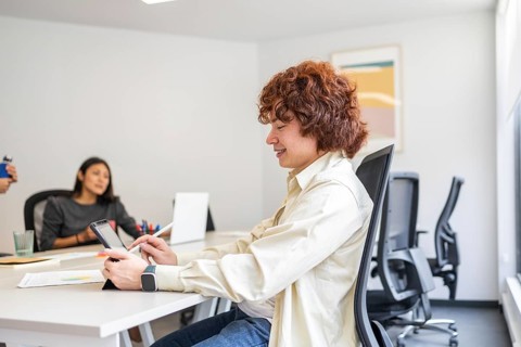A team of coworkers collaborating in a bright, modern office One person is focused on a tablet,