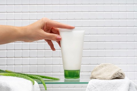 Cropped unrecognizable woman holding a tube of body care cream beside aloe gel in a bathroom, with