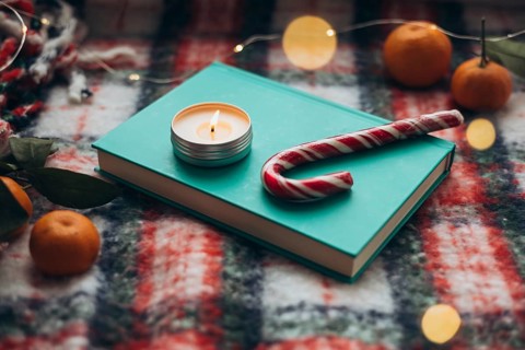 Cozy Christmas setting featuring a lit candle on a teal book, candy cane, and oranges surrounded by