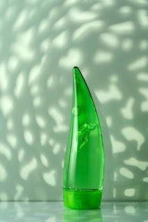 A translucent green aloe vera gel bottle on a white bathroom surface, highlighted by natural leafy