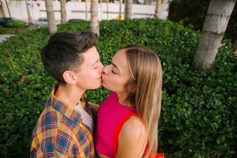 Happy lesbian couple sharing a kiss in a lush outdoor setting, celebrating love and diversity.