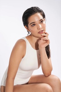 A fresh portrait of a young woman wearing a white bodysuit in a studio setting, gazing slightly