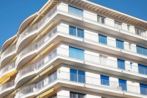 A modern apartment building features multiple curved balconies, white facade, and glass railings,