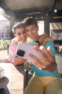 A joyful moment captured as a gay couple take a selfie at an outdoor cafe. They are embracing