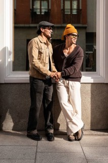 A Colombian couple stand outside in the city, sharing a moment of laughter. Dressed casually, they