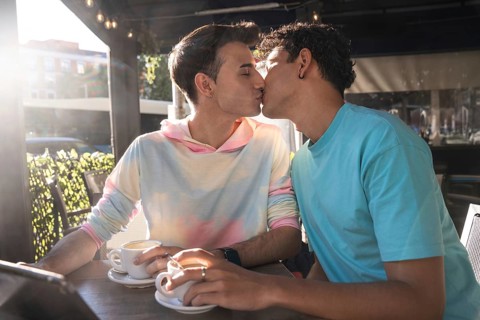 A loving gay couple shares a tender kiss while enjoying coffee at an outdoor cafe. Their connection
