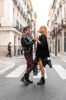 A joyful lesbian couple with unique styles, holding hands and smiling on a lively city street,