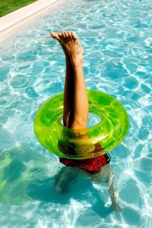 A person playfully balances upside down in a swimming pool, legs pointing skyward through a bright