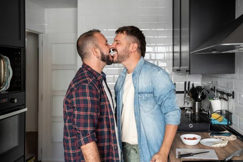 A joyful gay couple in a kitchen, playfully sharing cream from a dessert, showcasing love and