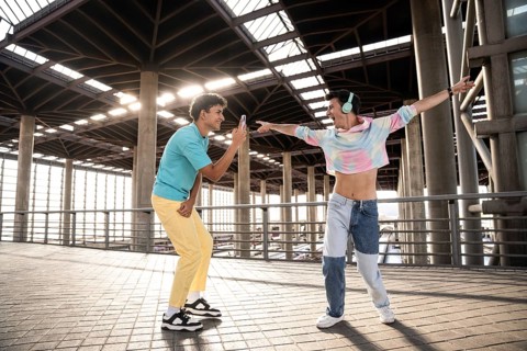 A lively gay couple enjoys a playful moment in an urban setting. One person, wearing colorful