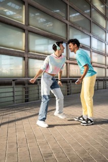 A happy couple shares a joyful moment outdoors, dressed in colorful, casual outfits. Smiling and