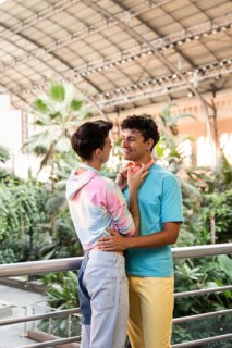 A cheerful gay couple embracing in a lush indoor garden. Their colorful outfits and vibrant