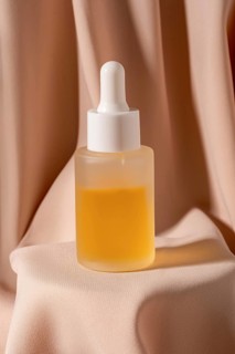 A minimalist flat lay photo featuring a glass dropper bottle of golden skincare The bottle is