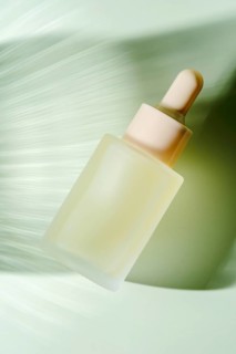 A frosted glass serum dropper bottle hovers against a blurred green background, depicting motion