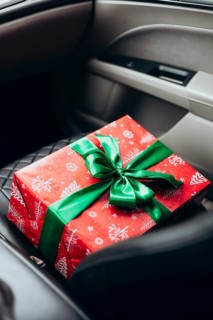 A beautifully wrapped red gift with a green ribbon rests on a car seat, capturing the anticipation