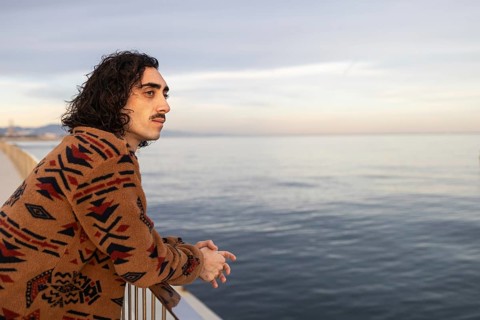 A man with a thoughtful expression leans against a railing, gazing at the tranquil sea The natural