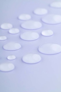Close-up image of droplets scattered on a smooth, lavender-colored surface The droplets vary in