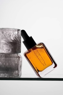 Aesthetic close-up of a vitamin C serum in a clear pipette bottle resting against ice blocks on a